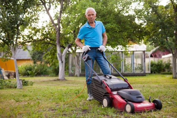 Positive elderly man with lawnmower when mowing the lawn