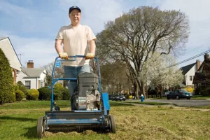 Mature man pushing gas power rake. De-thatching front yard.