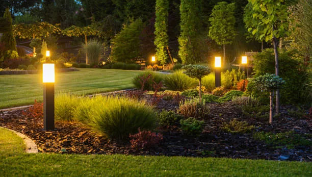 Panoramic Photo of LED Light Posts Illuminated Backyard Garden During Night Hours. Modern Backyard Outdoor Lighting Systems.