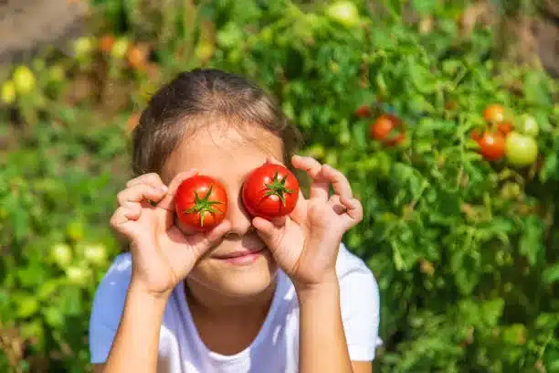 A young girl holding tomatoes in front of her eyes like binoculars